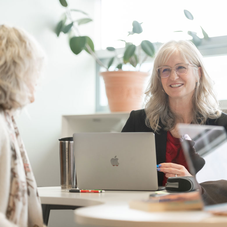 A UBCO professor and staff member chatting at a desk.