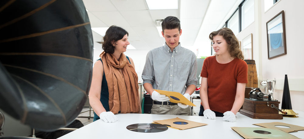 Prof. Brigitte Le Normand converses with two students in a humanities lab