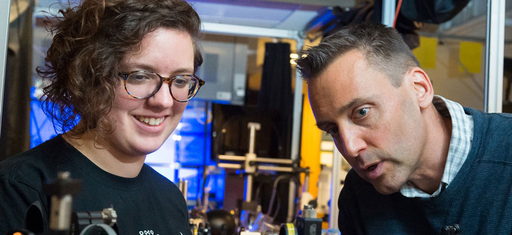 Professor Jonathan Holzman and a student inspect laser equipment.