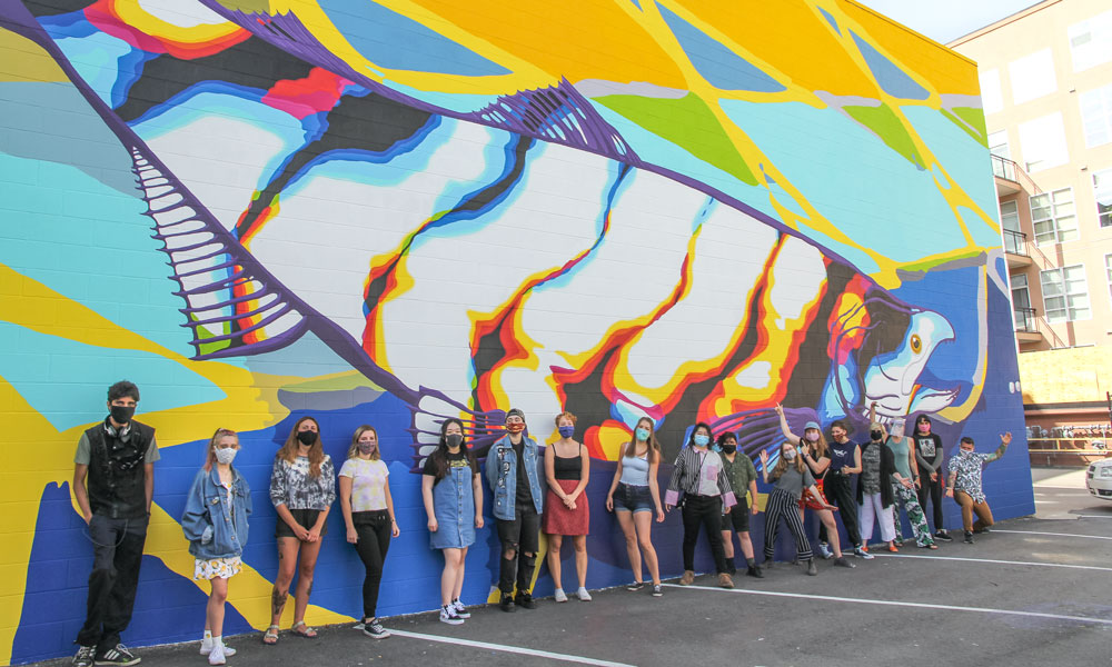students standing in front of a bright fish mural