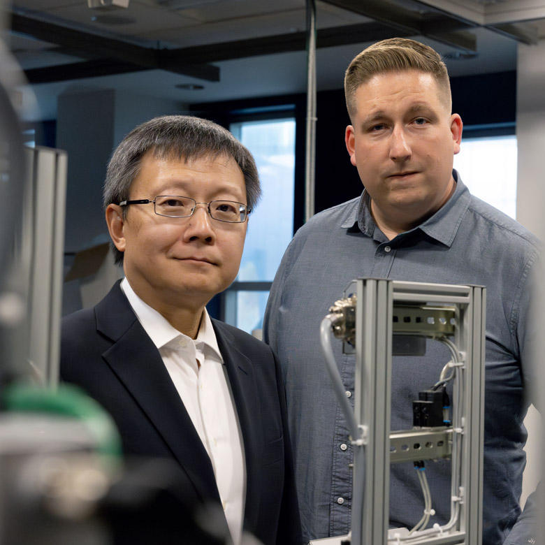 Dr. Zheng Liu and UBC alum Jozsef Hamari standing amidst techy-looking stuff in a lab