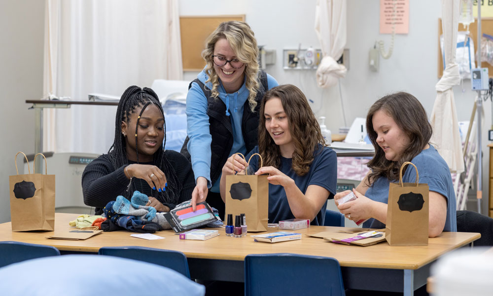 Four female nursing students are gathered around a table covered with socks, nail files and other foot-related items. The students are putting the items into small 'goody bags'.