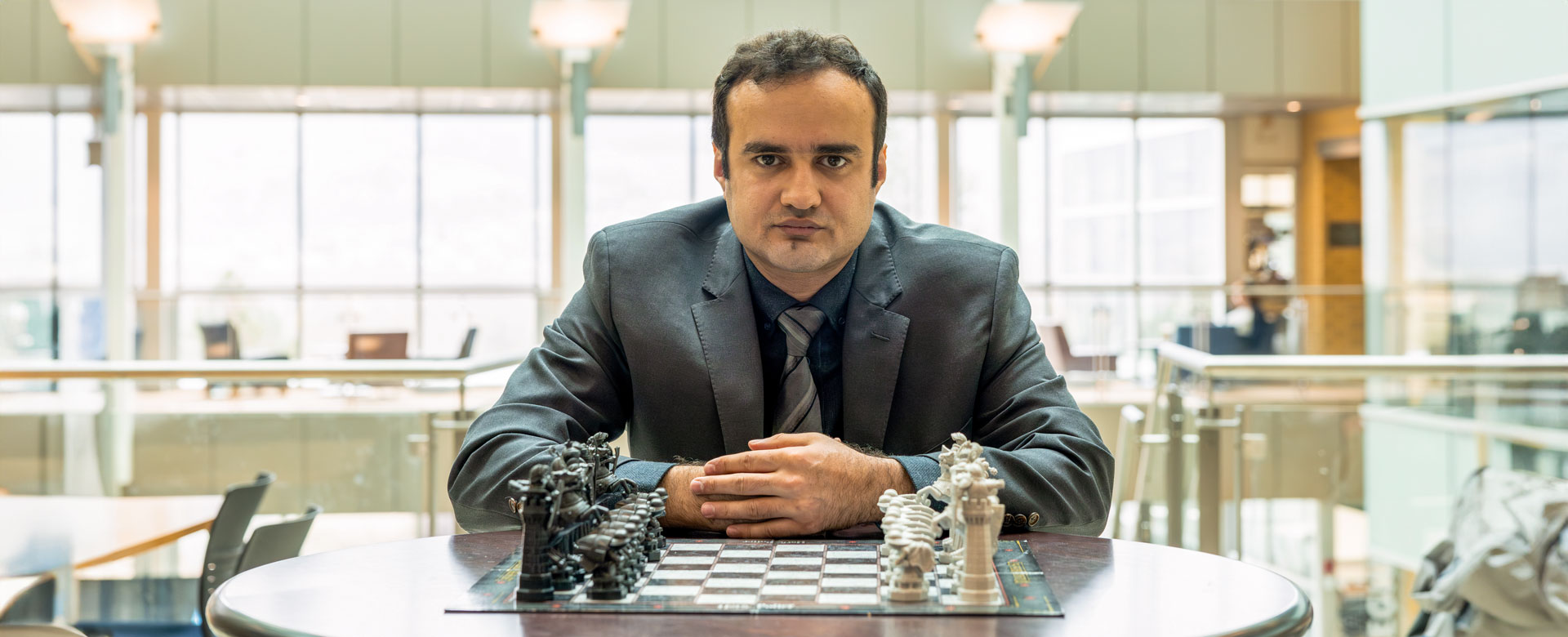 Dr. Amir Ardestani-Jaafari sits in front of a chess board with his hands clasped together, looking intently at the camera.