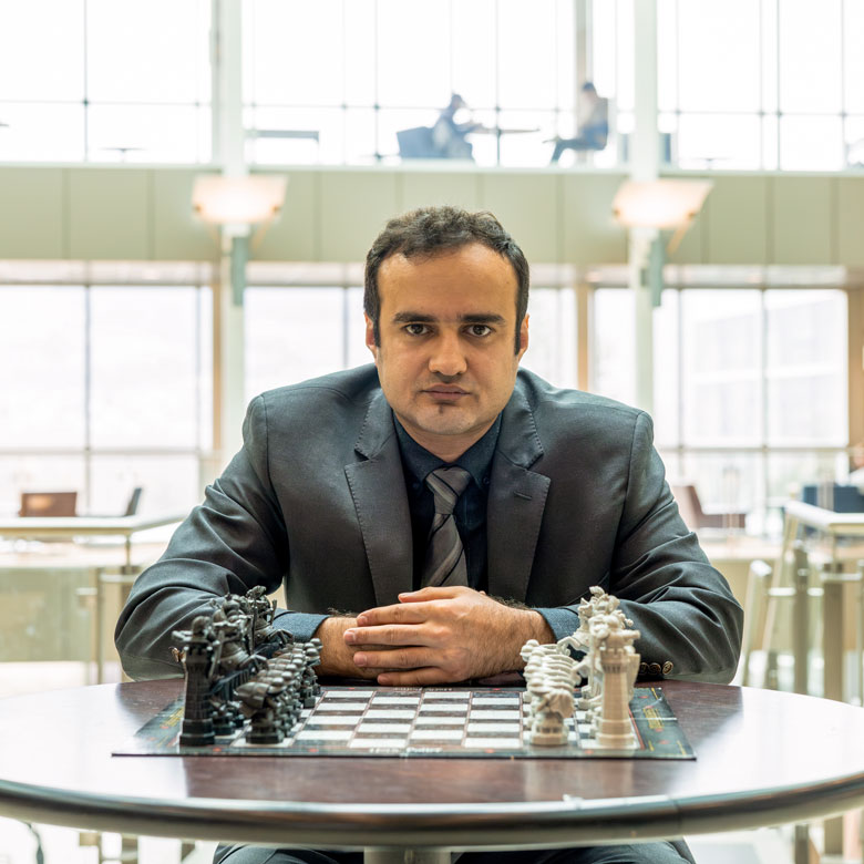 Dr. Amir Ardestani-Jaafari sits in front of a chess board with his hands clasped together, looking intently at the camera.